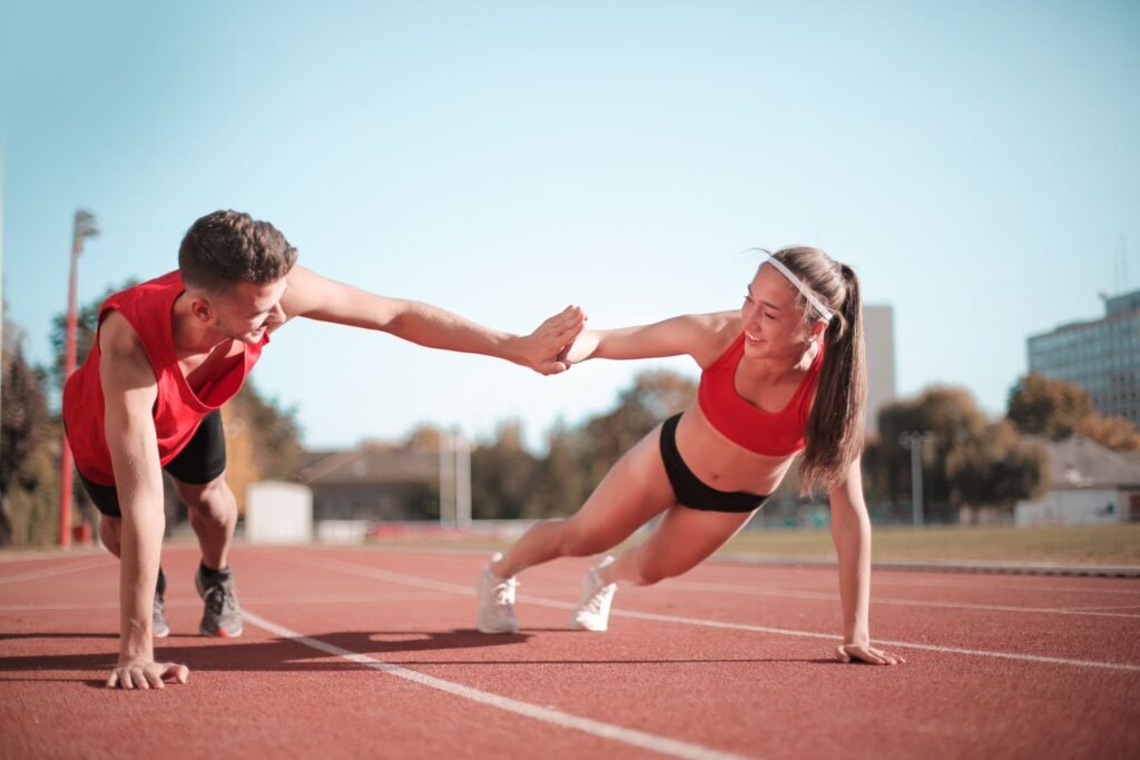 Pareja entrena al aire libre haciendo planking sobre un circuito de atletismo. Disfrutan de un sistema inmunológico fuerte.